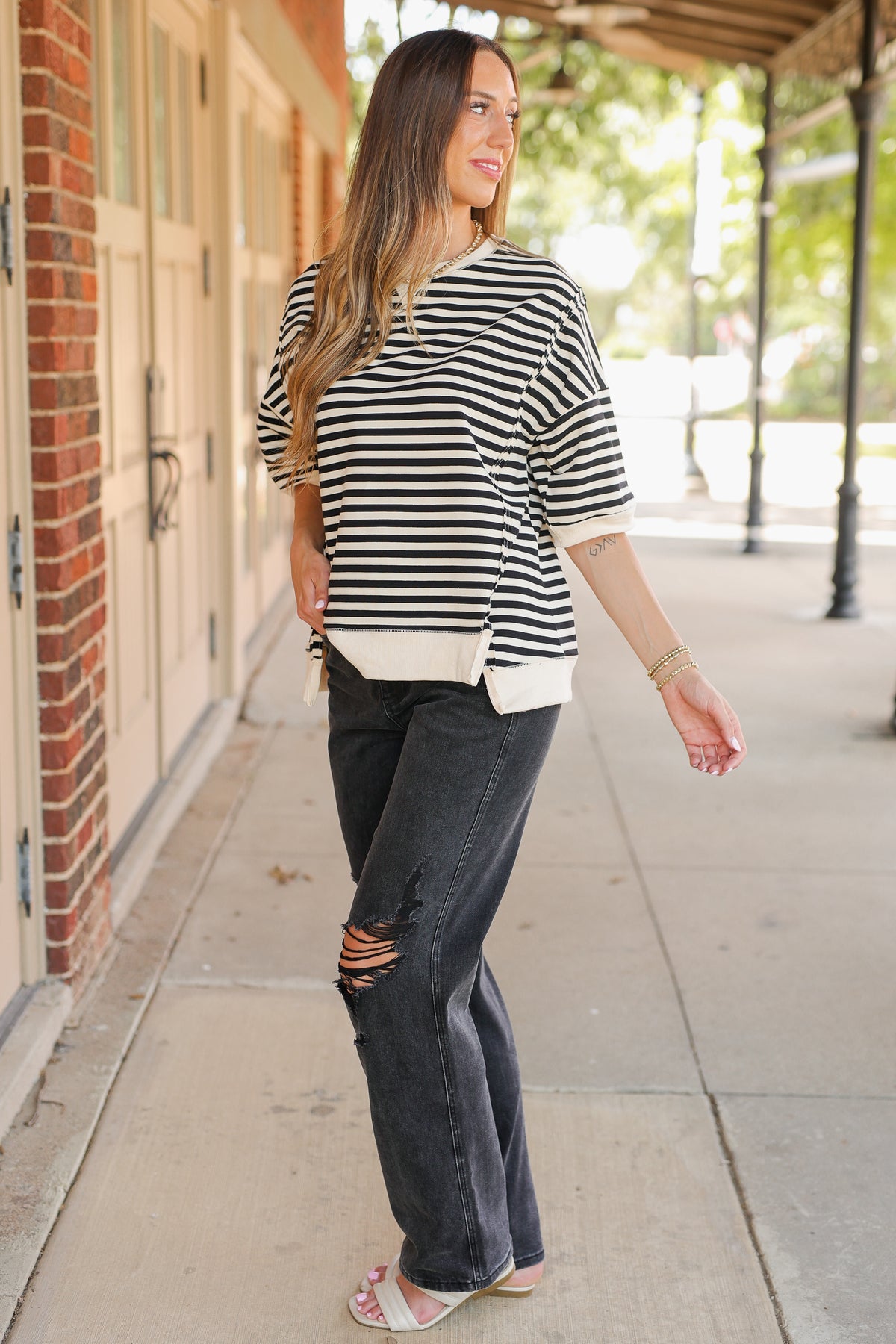 Woman wearing a black and white striped shirt and ripped jeans on a sidewalk.