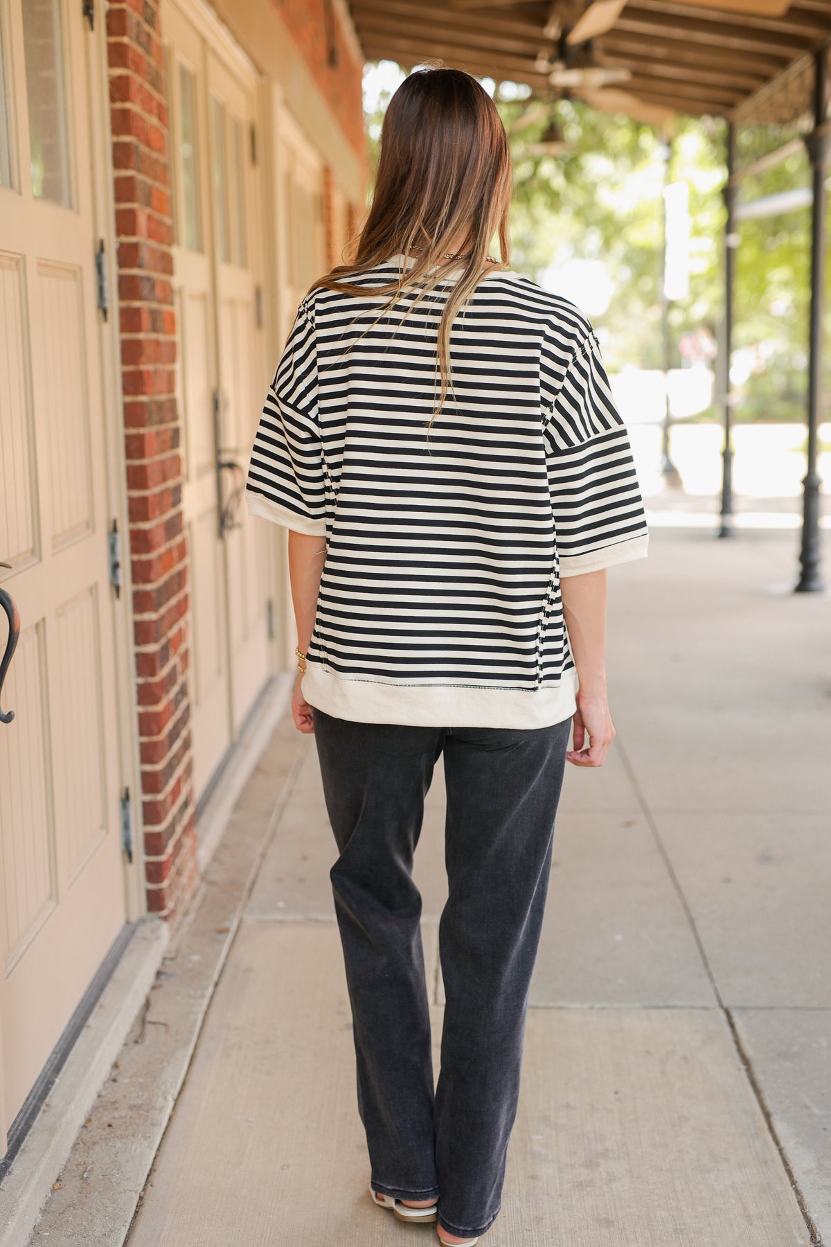 Person wearing a black and white striped shirt and dark pants walking on a sidewalk.