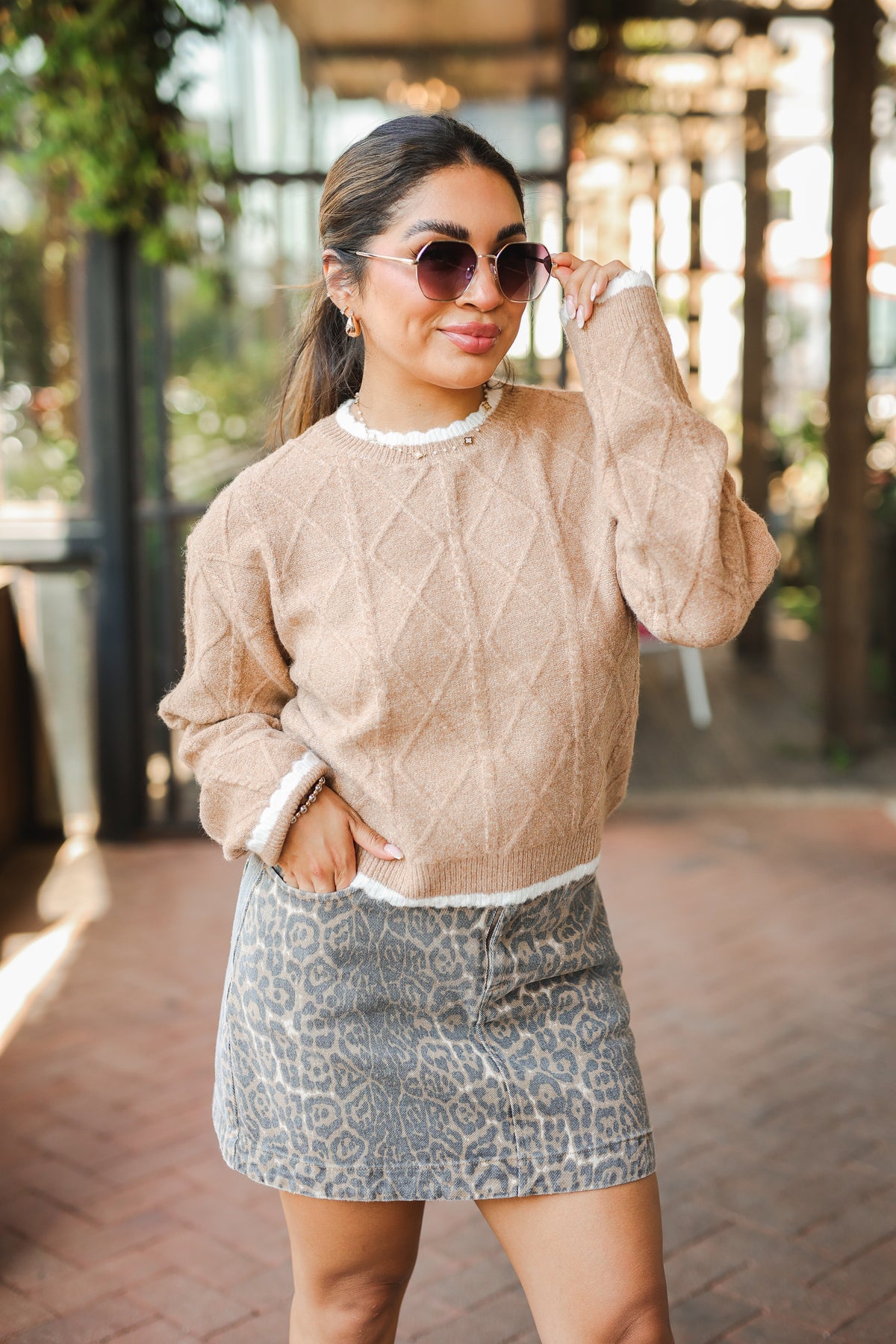 Woman wearing a beige sweater and patterned skirt outdoors