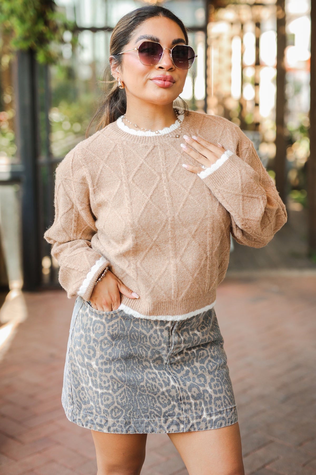 Woman wearing a beige sweater and patterned skirt outdoors