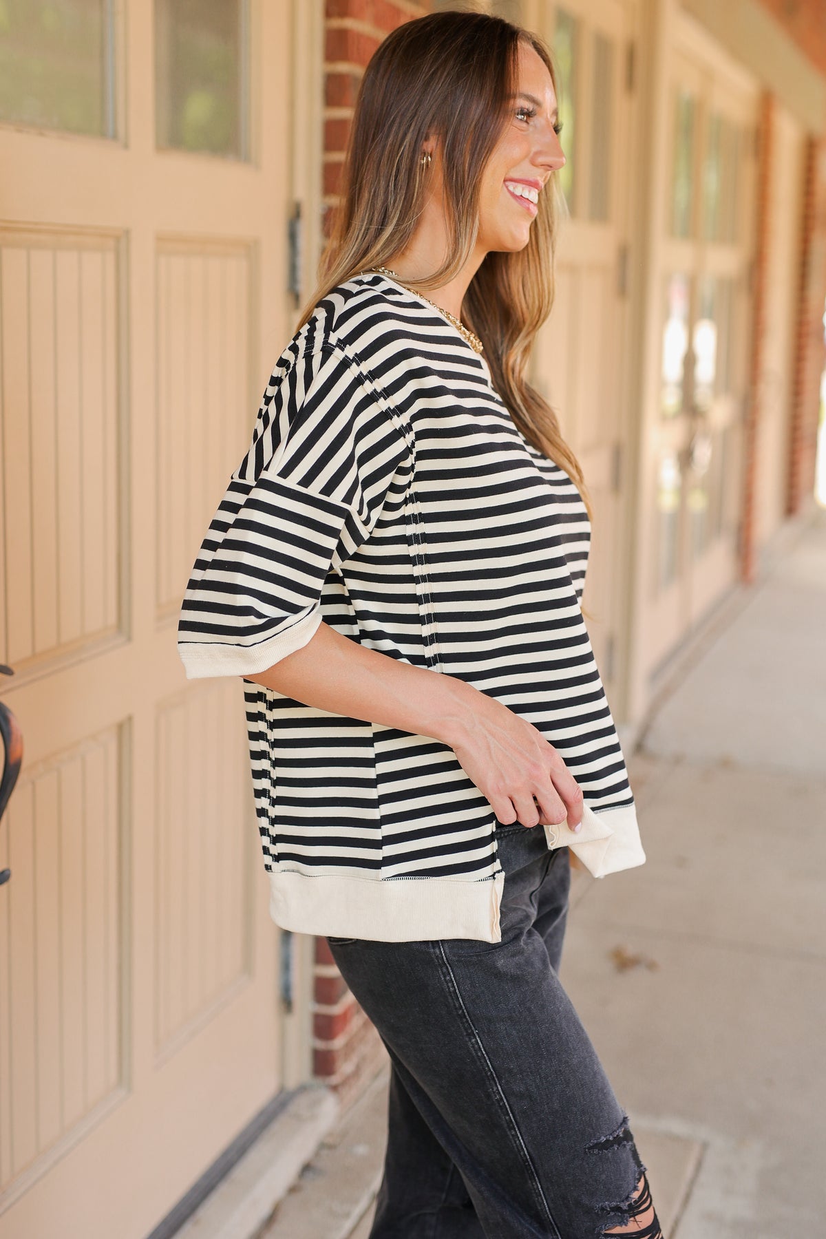 Woman wearing a black and white striped shirt and dark jeans, standing on a porch.