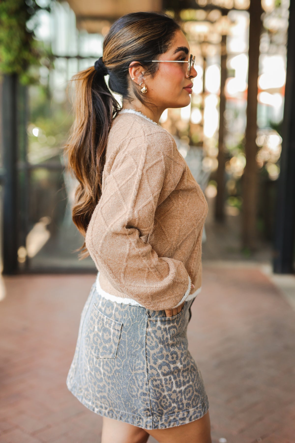 Woman wearing a beige sweater and leopard print skirt outdoors