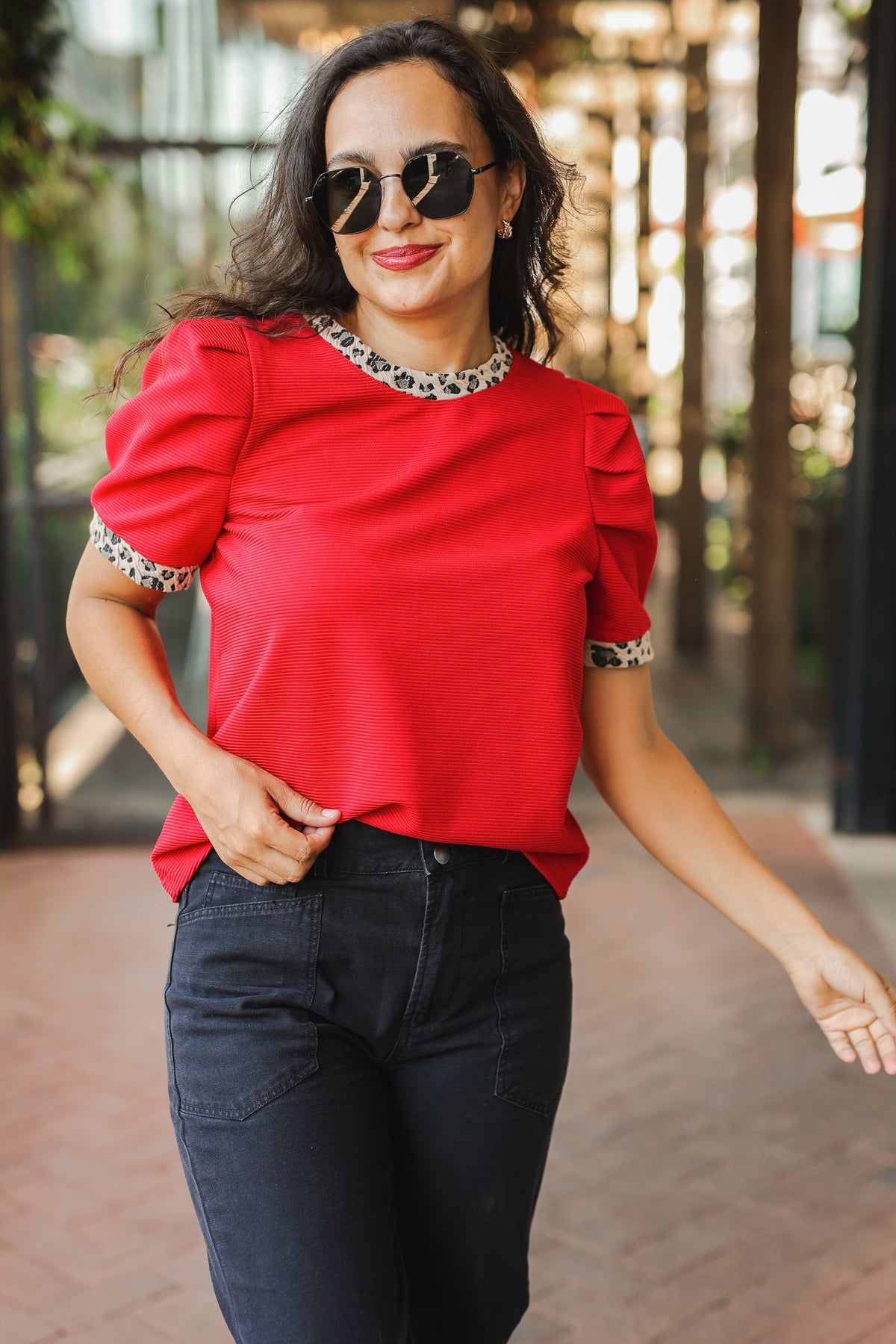 Woman wearing a red top with puffed sleeves and black pants outdoors.