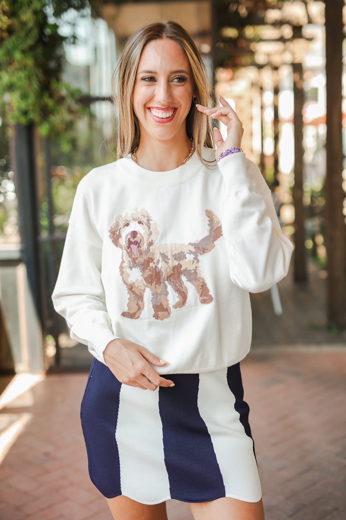 Woman wearing a white sweatshirt with a dog design and a navy and white skirt outdoors.