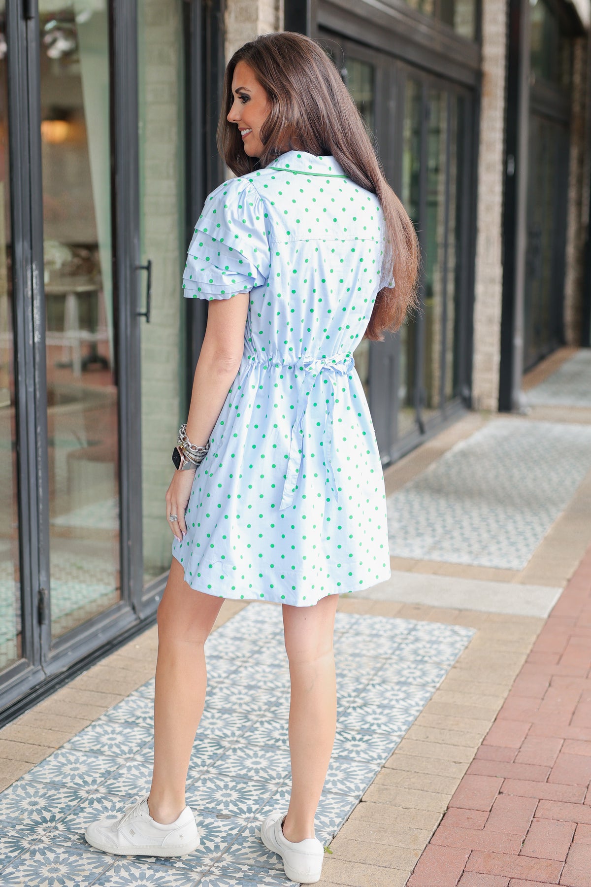 Woman in a light blue polka dot dress walking on a sidewalk.