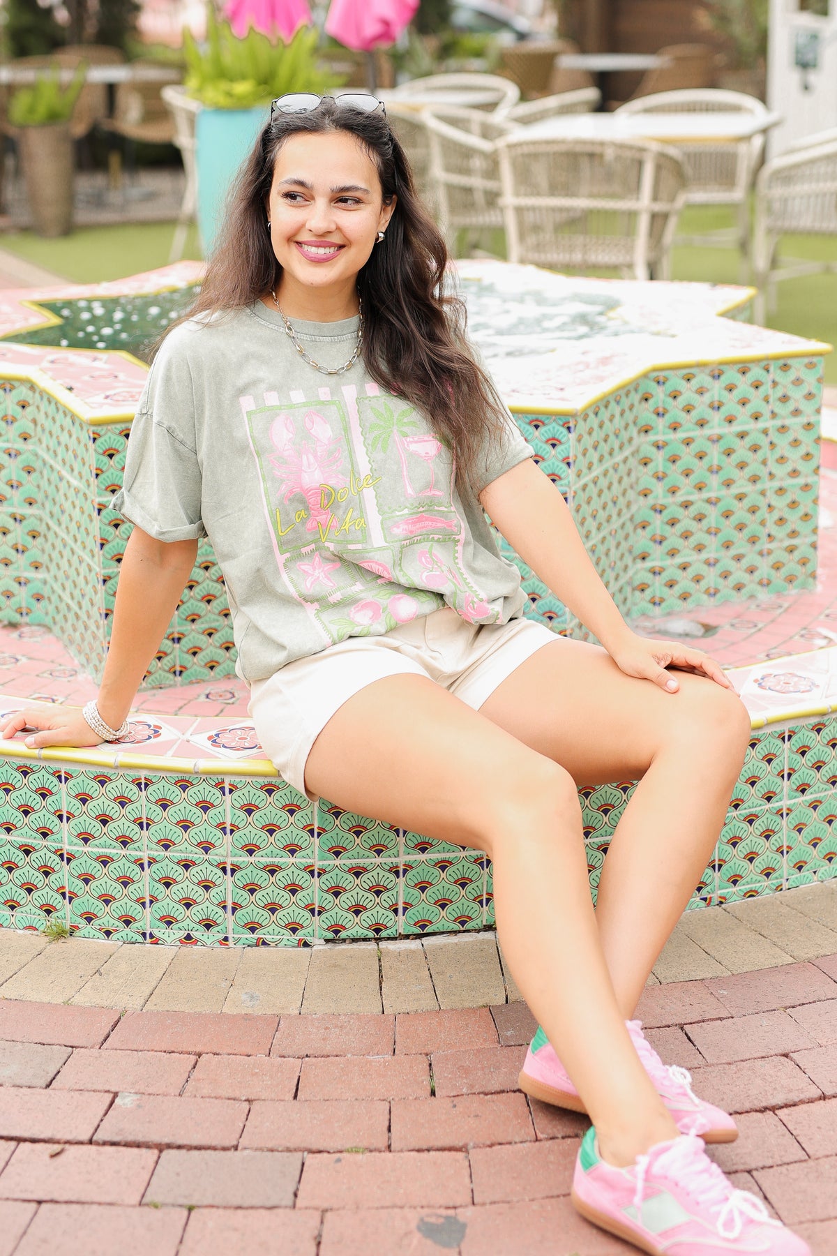 Woman sitting on a patterned bench outdoors with tables and chairs in the background