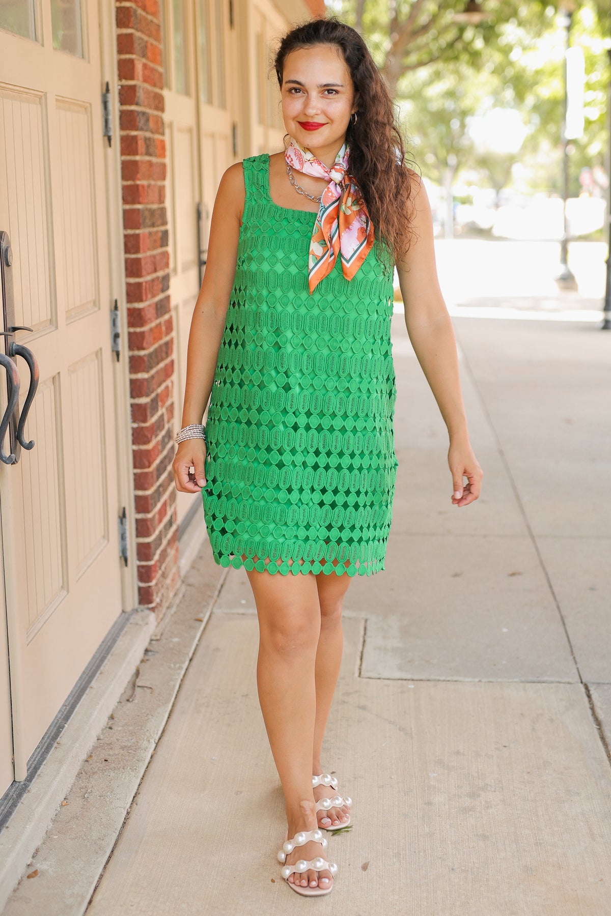 Woman in a green dress standing on a sidewalk next to a building.