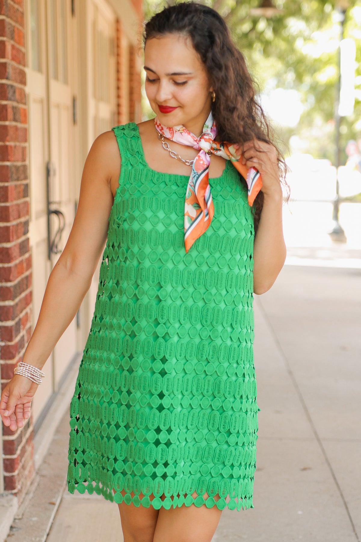 Woman wearing a green dress with a colorful scarf, standing on a sidewalk.