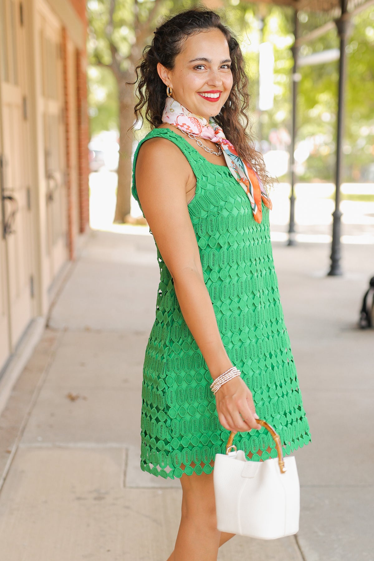 Woman wearing a green dress with a white handbag on a sidewalk.