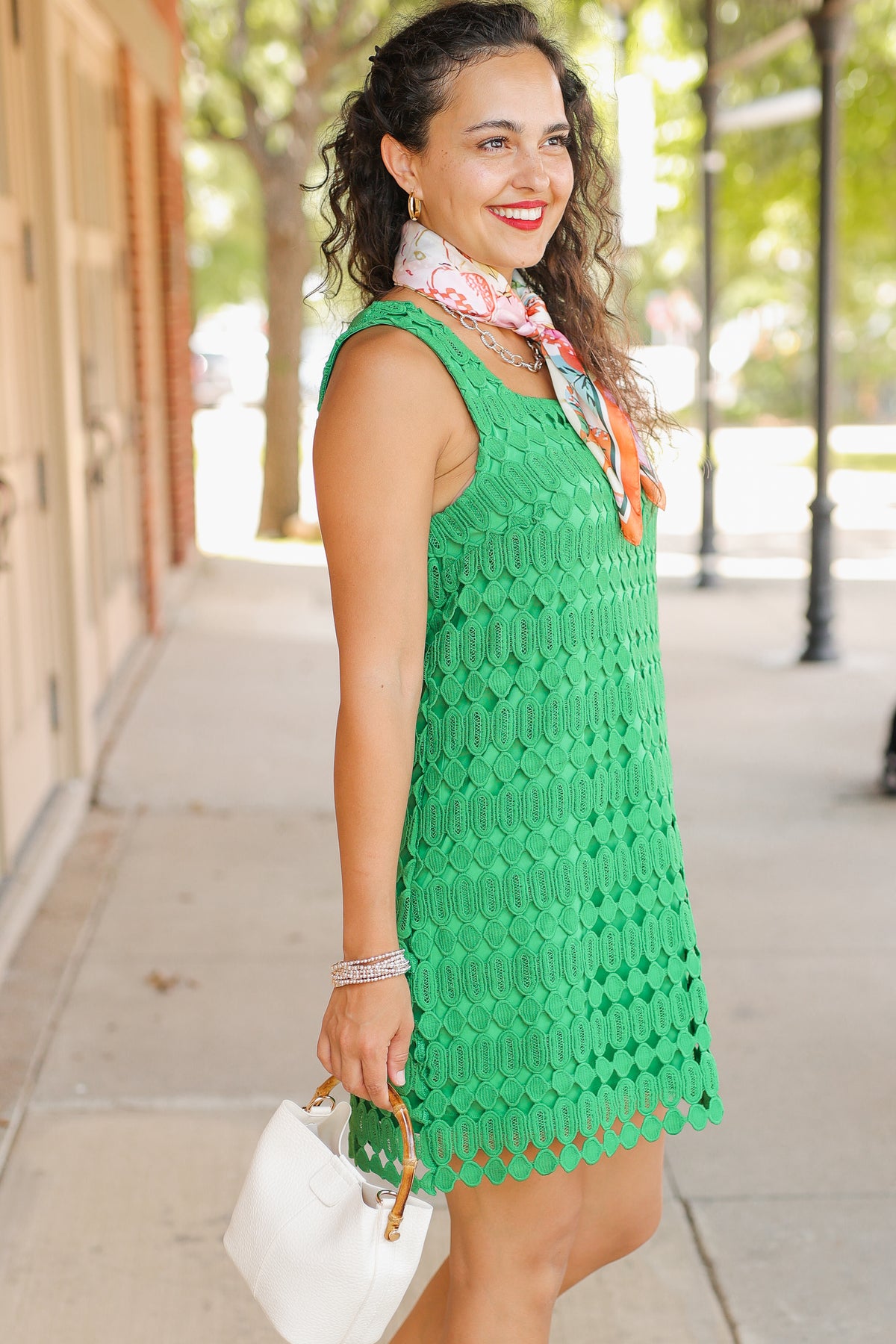 Woman in a green dress standing on a sidewalk with trees and buildings in the background