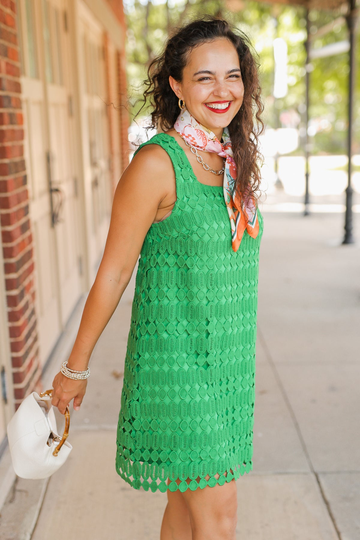Woman in a green dress with a colorful scarf, standing on a sidewalk.