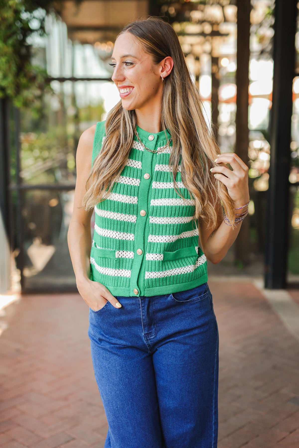 Woman wearing a green and white striped vest with blue jeans outdoors.