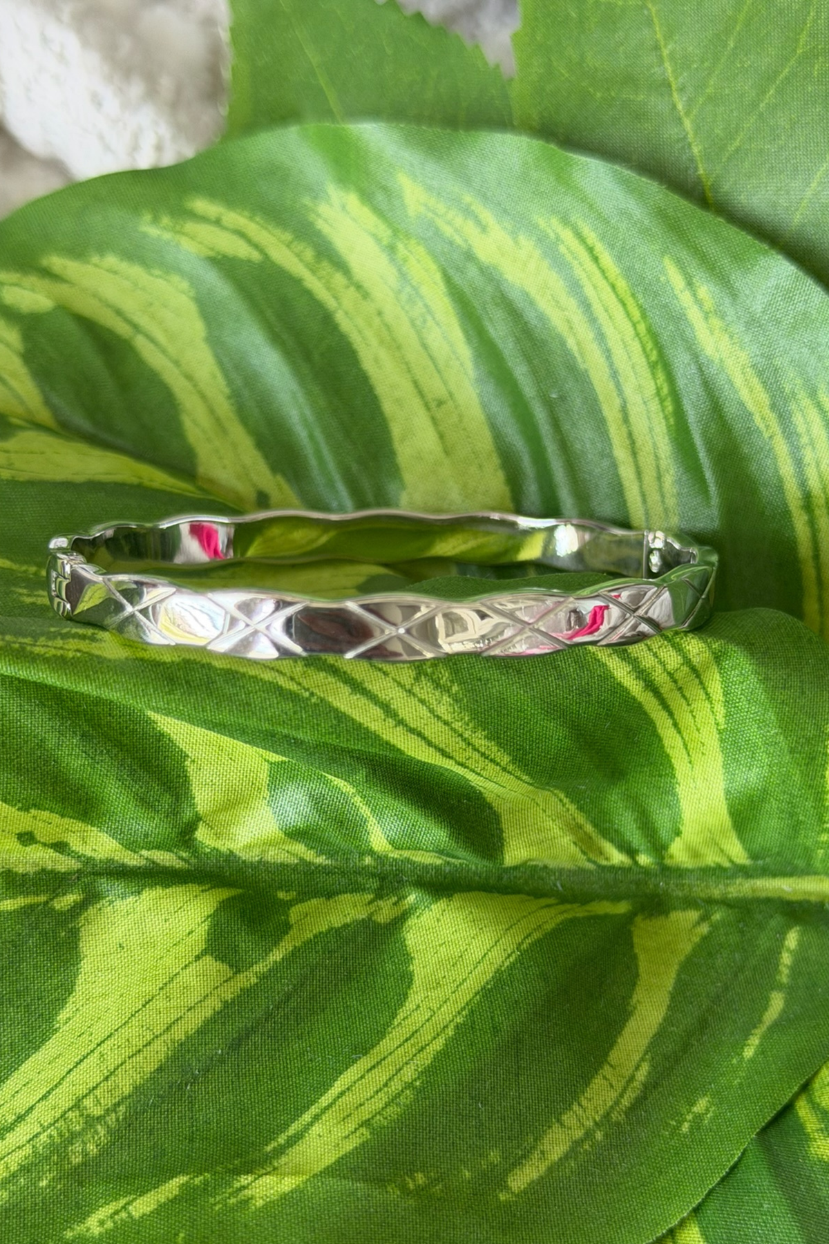 Silver bracelet with geometric pattern on green leaves