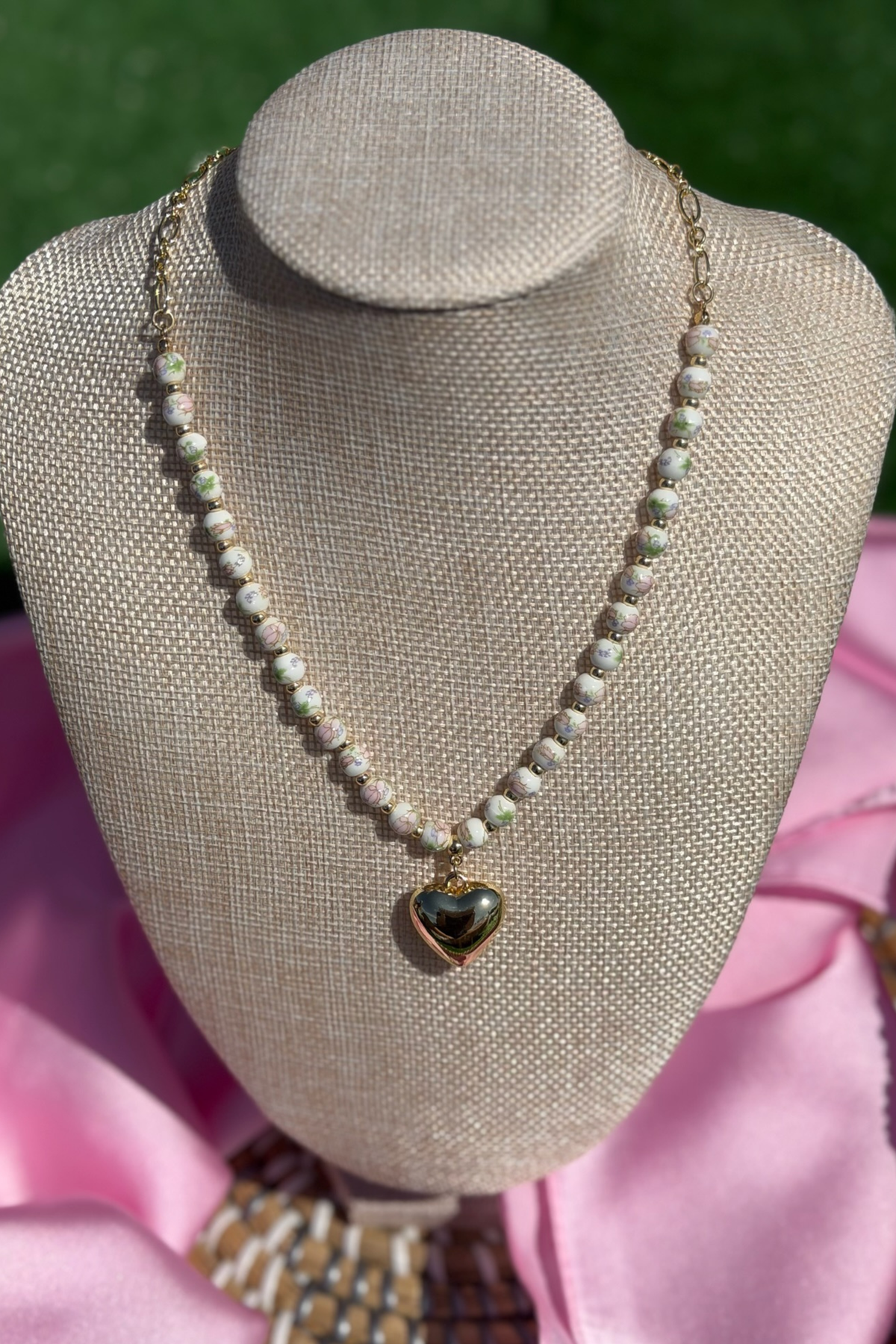 Pearl necklace with a heart-shaped pendant on a mannequin bust against a pink fabric background.