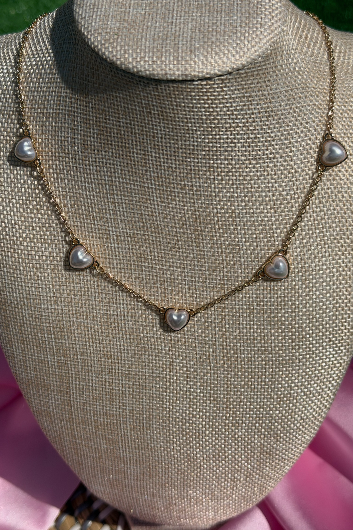 Necklace with heart-shaped pendants on a mannequin bust against a pink fabric background