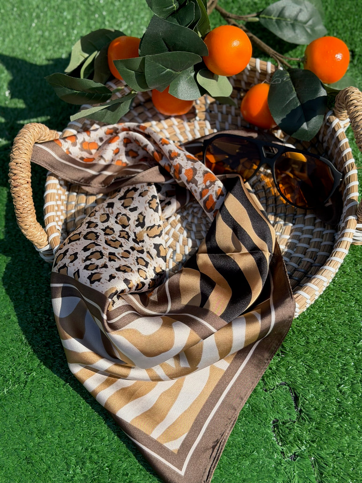 Patterned scarf, sunglasses, and basket with oranges on a green surface