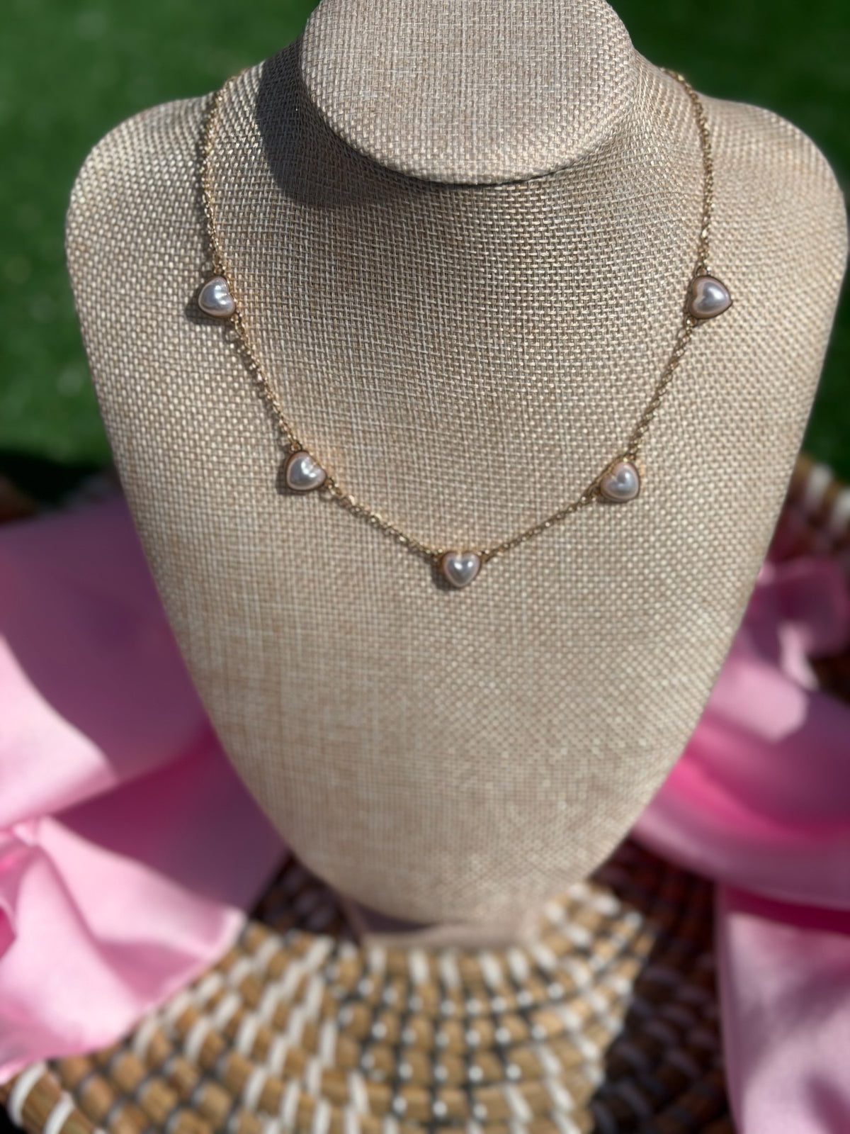 Necklace with heart-shaped pendants on a mannequin bust against a pink and green background