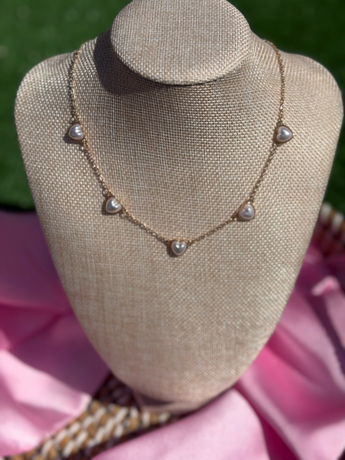 Necklace with heart-shaped pendants on a mannequin bust against a pink fabric background