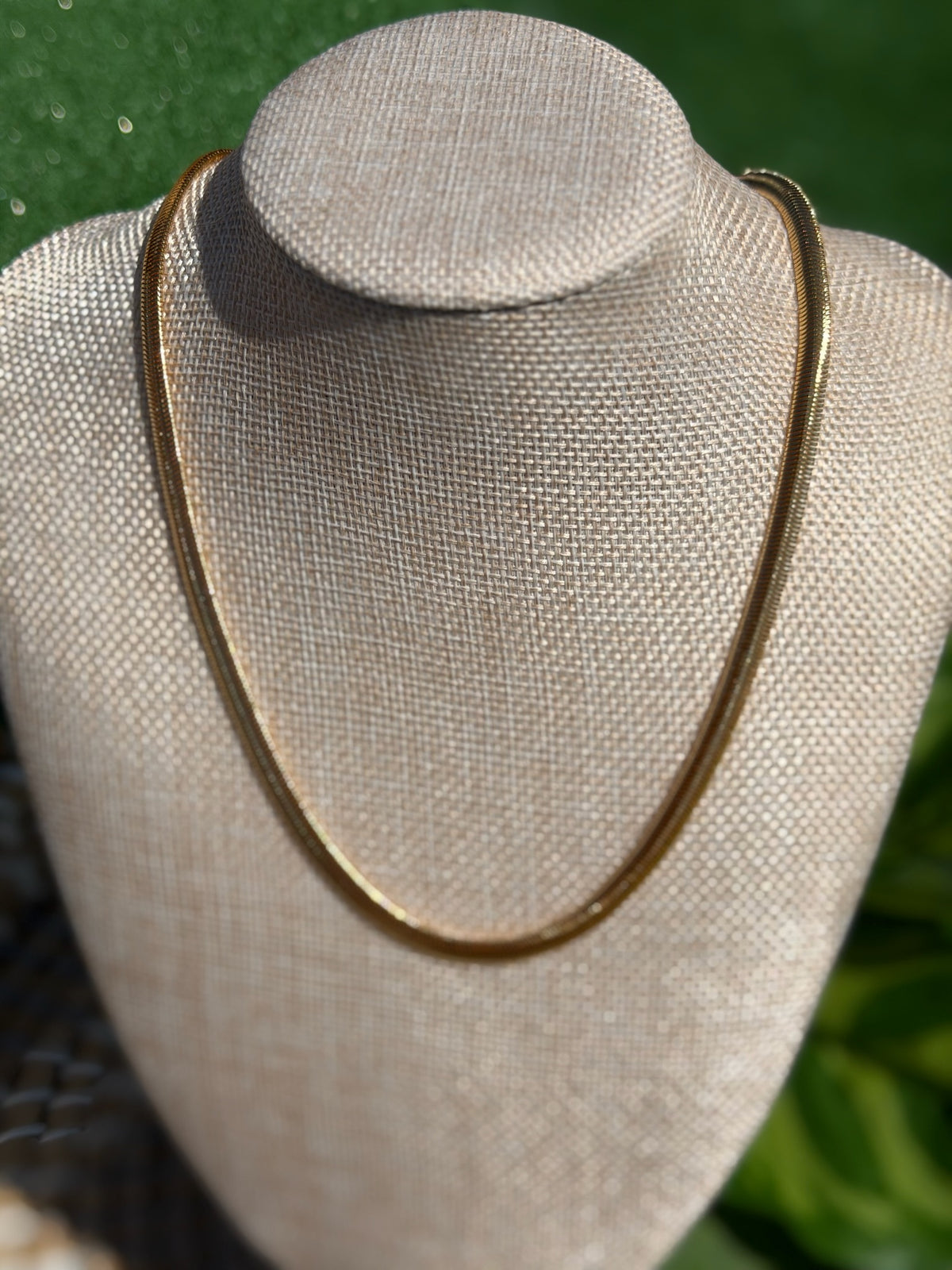 Gold necklace on a mannequin bust with a blurred green background