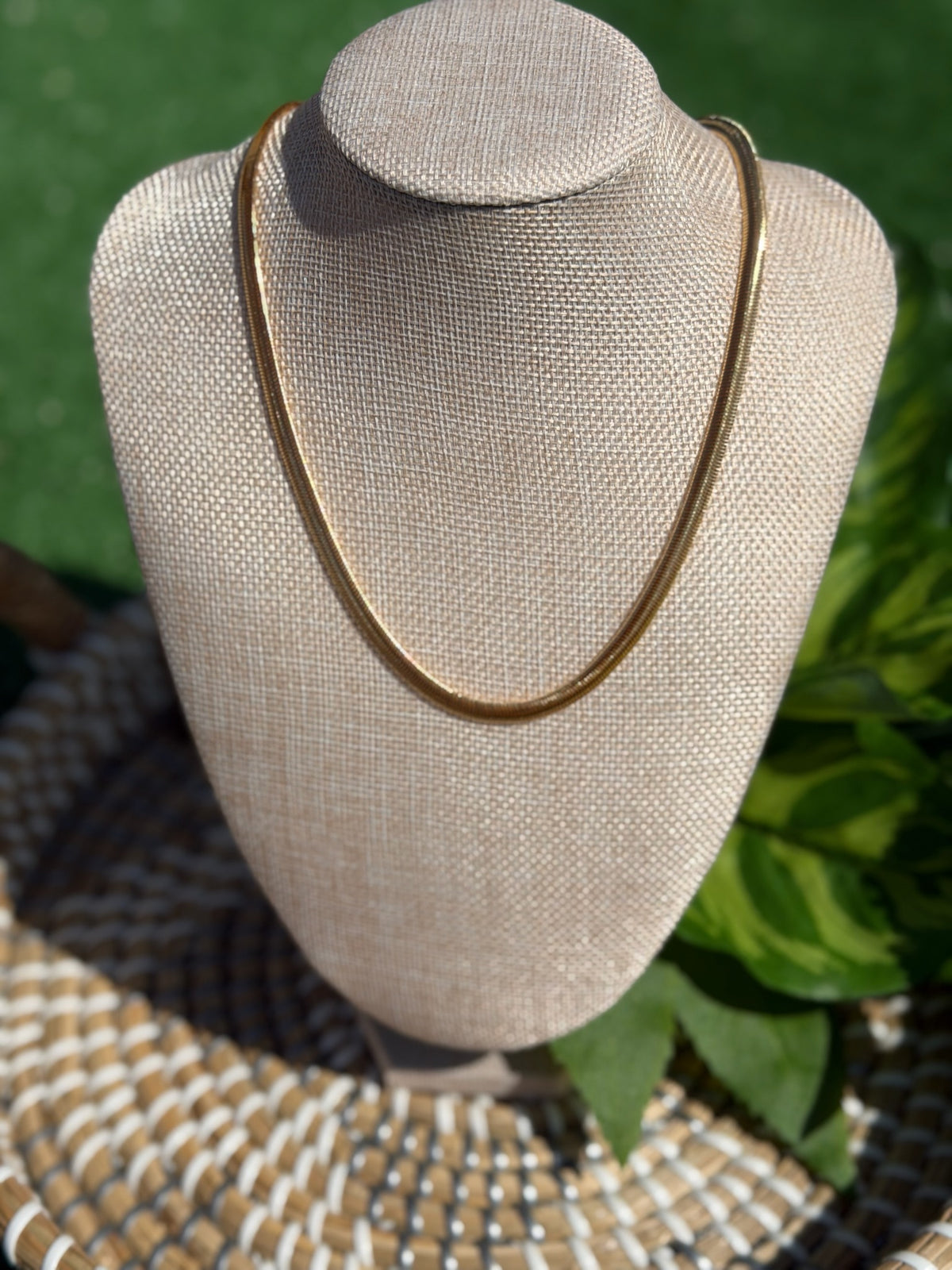 Gold necklace on a mannequin bust with a blurred green background