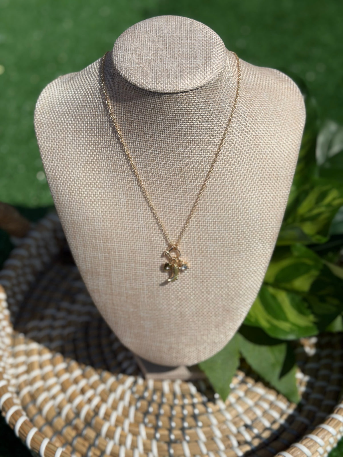 Gold necklace with a pendant on a mannequin bust against a green leafy background