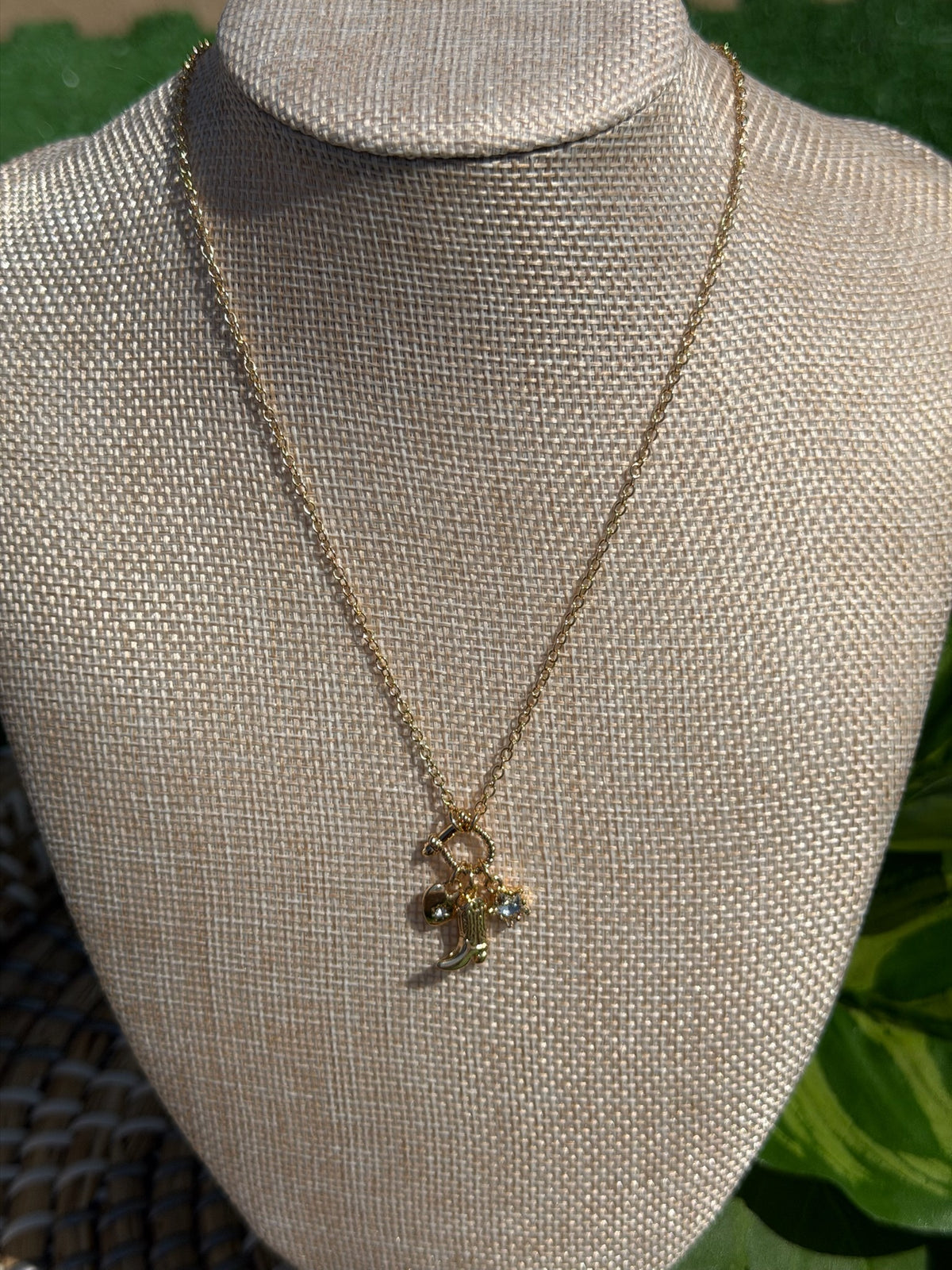 Gold necklace with a pendant on a mannequin bust against a green leafy background