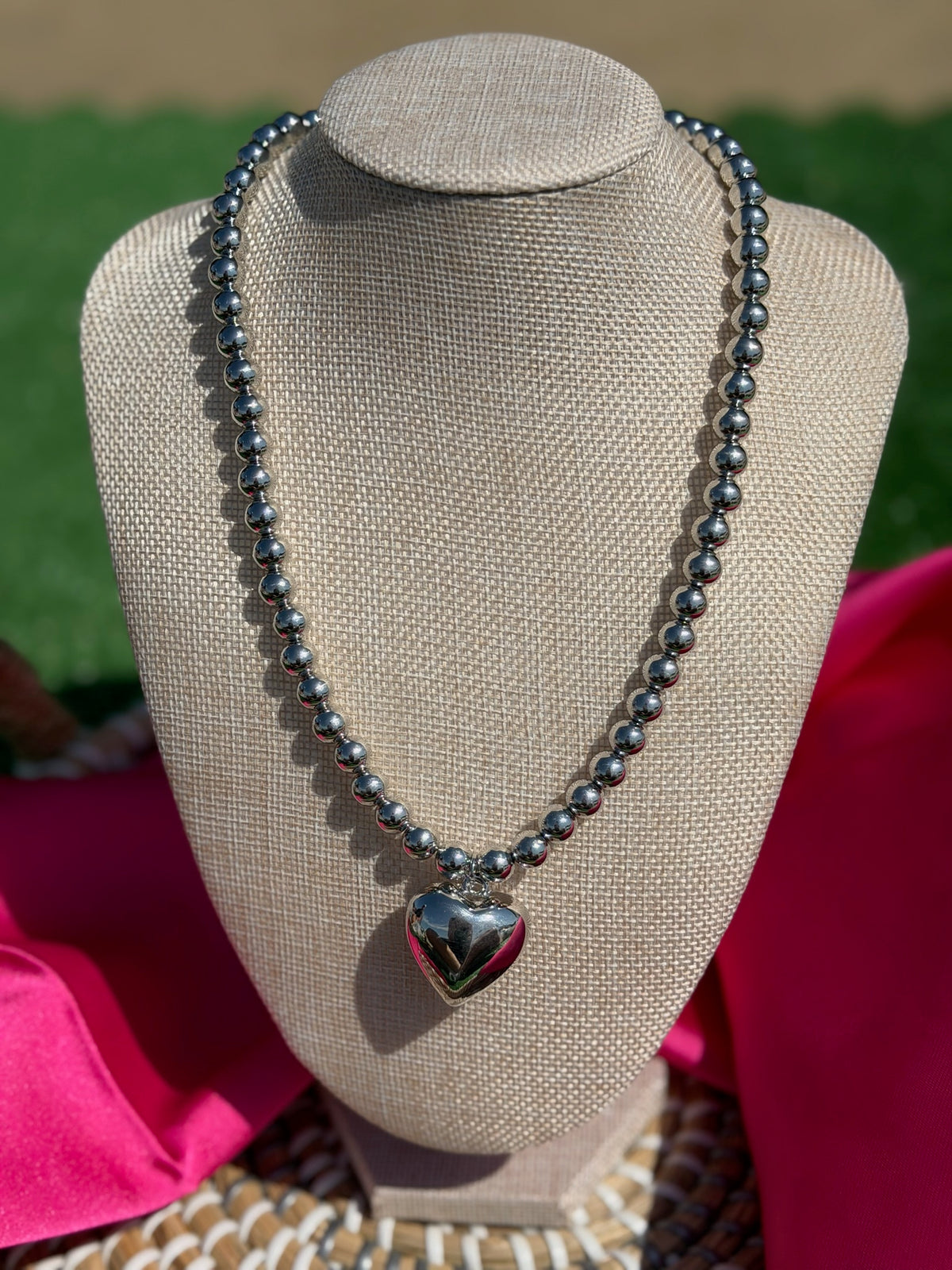 Necklace with a heart pendant on a mannequin bust against a pink and green background