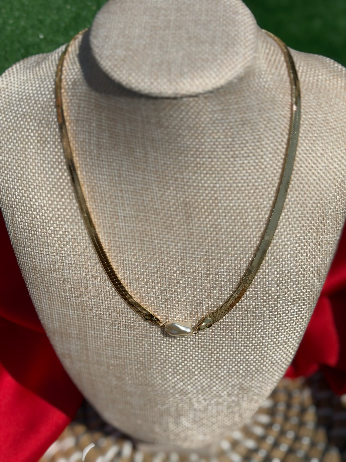 Necklace on a mannequin bust with a red garment and patterned fabric in the background