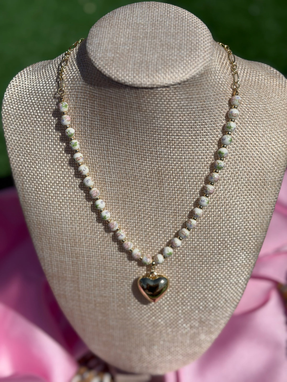 Necklace with a heart pendant on a mannequin bust against a pink and green background