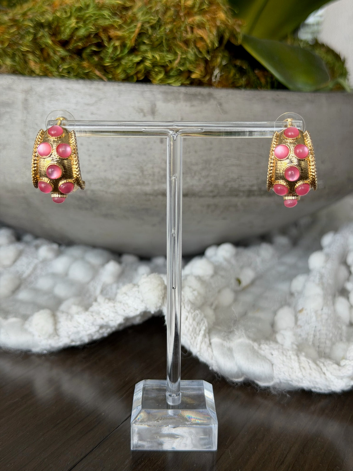 Gold and pink earrings on a clear stand with a natural background