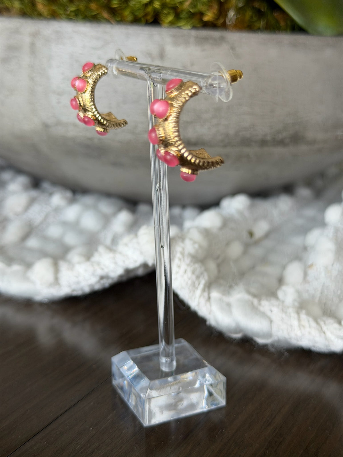 Gold earrings with pink beads on a clear stand against a blurred natural background