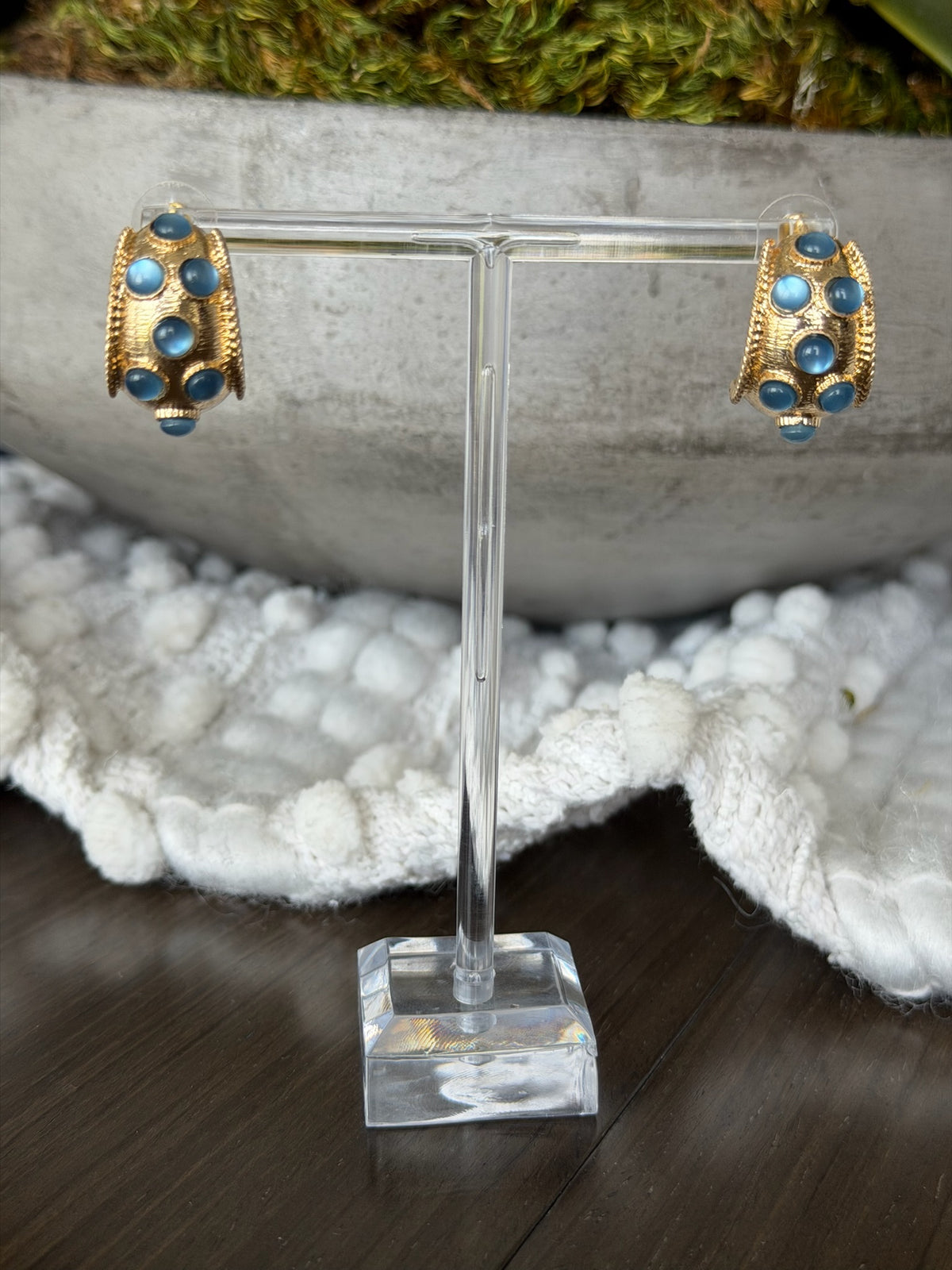Gold and turquoise earrings on a clear stand with a natural background