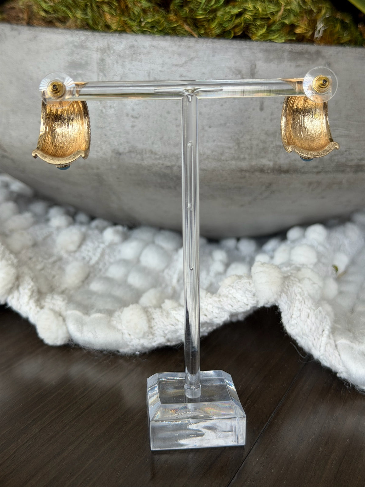 Gold acorn-shaped earrings on a clear stand with a natural background