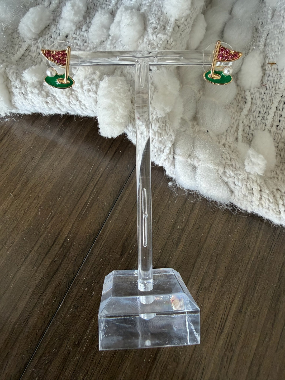 Golf-themed earrings on a clear stand with a textured white surface in the background