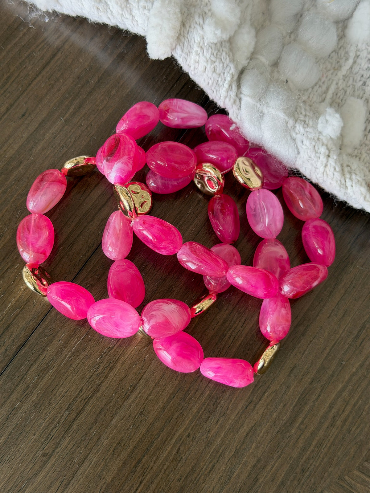 Pink beaded bracelet with gold accents on a wooden surface
