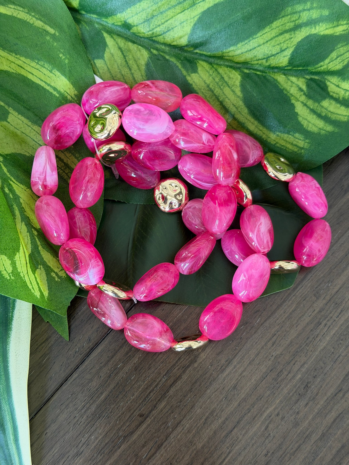 Pink beaded bracelet with gold accents on a green leafy background