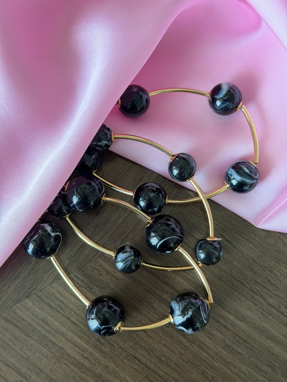 Gold hoop earrings with black beads on a pink and wooden surface