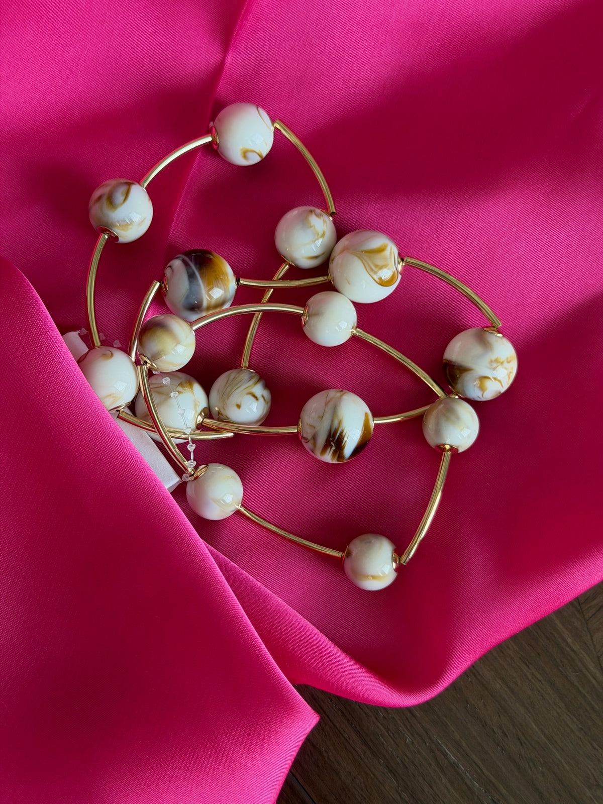 Gold bracelet with white beads on a pink fabric background