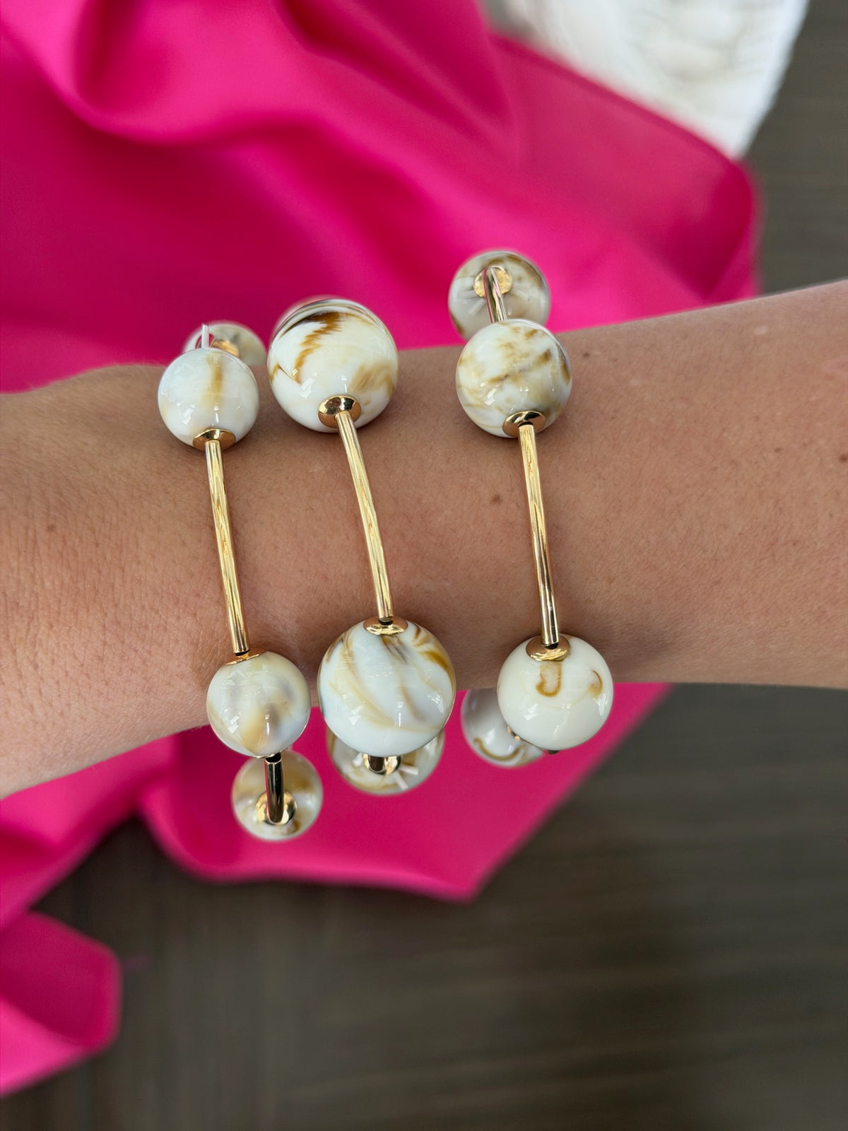 Bracelet with white and gold beads on a wrist against a pink fabric background