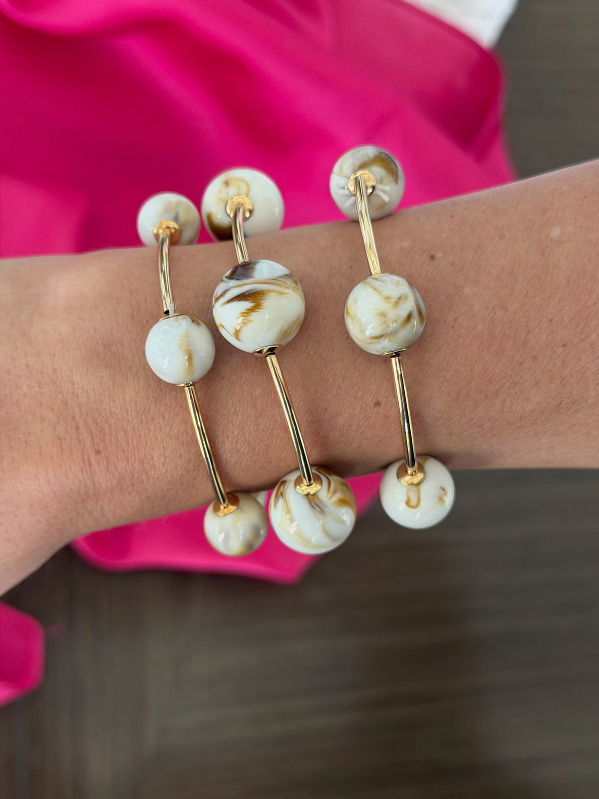 Bracelet with white marbled beads and gold accents on a wrist against a pink background