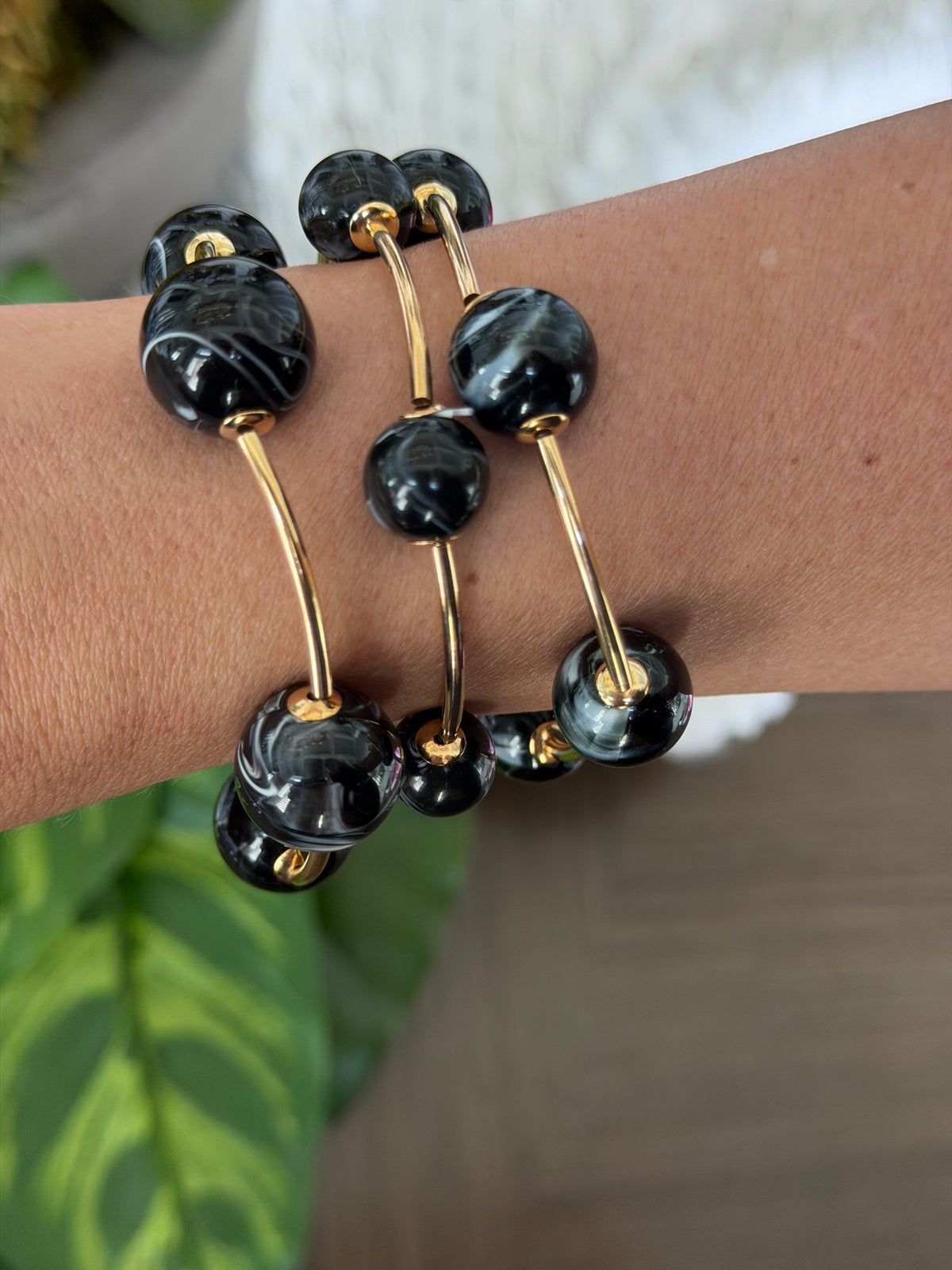 Black beaded bracelet with gold accents on a wrist, blurred green plant in the background