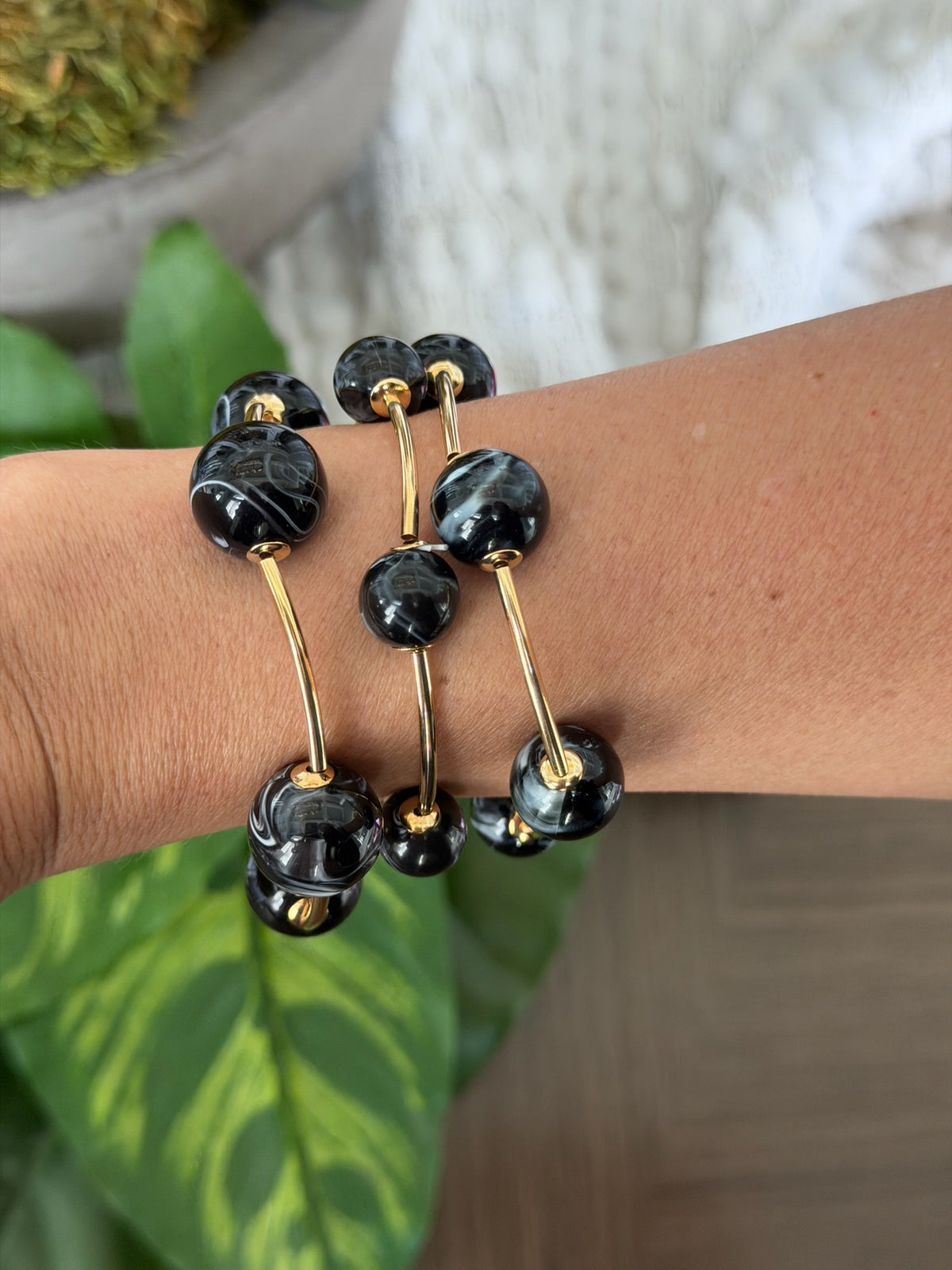 Black beaded bracelet with gold accents on a wrist, with green leaves and a blurred background