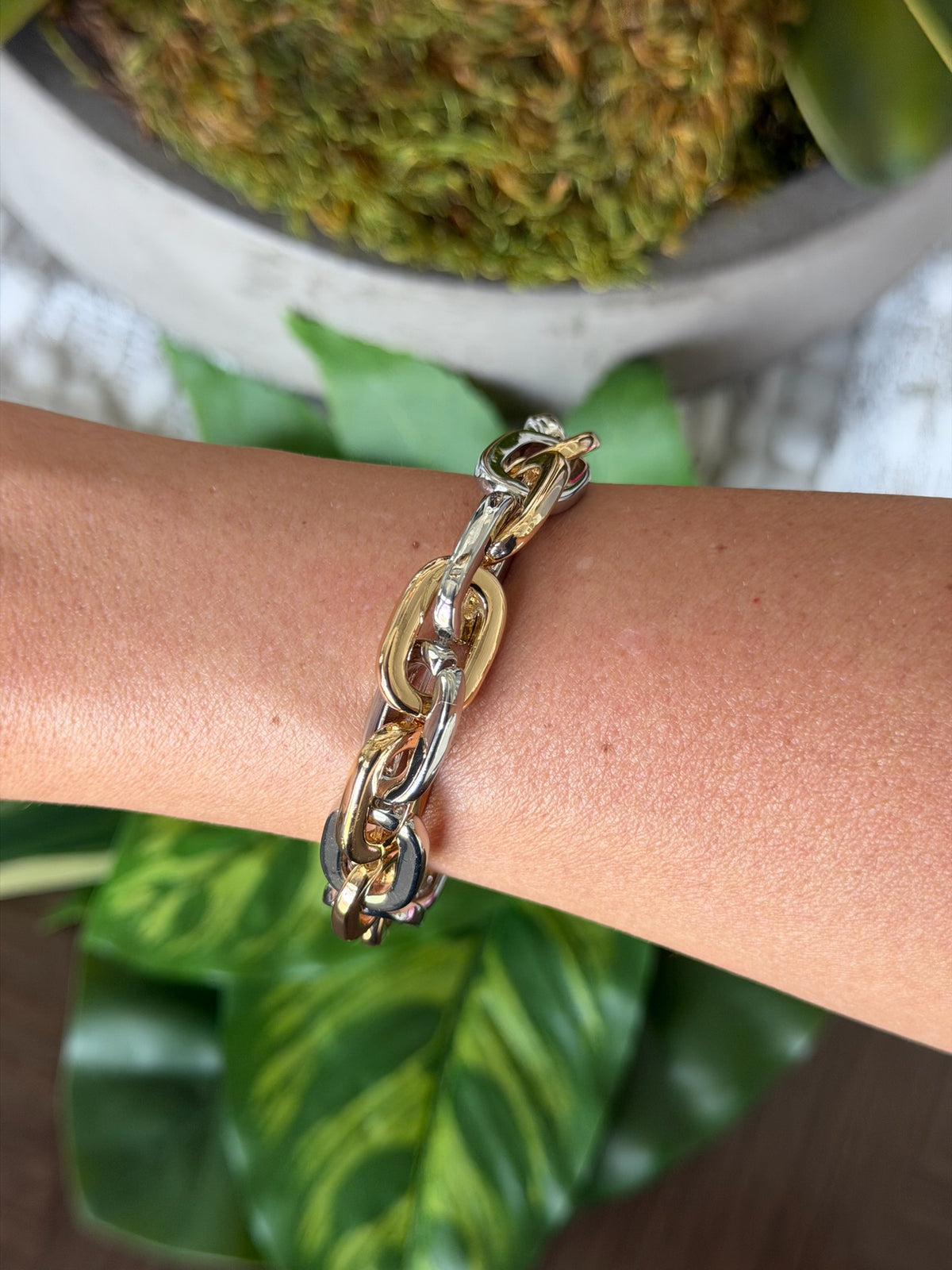 Gold chain bracelet on a wrist with a blurred green plant background