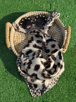 Leopard print scarf and sunglasses on a woven basket with green grass background