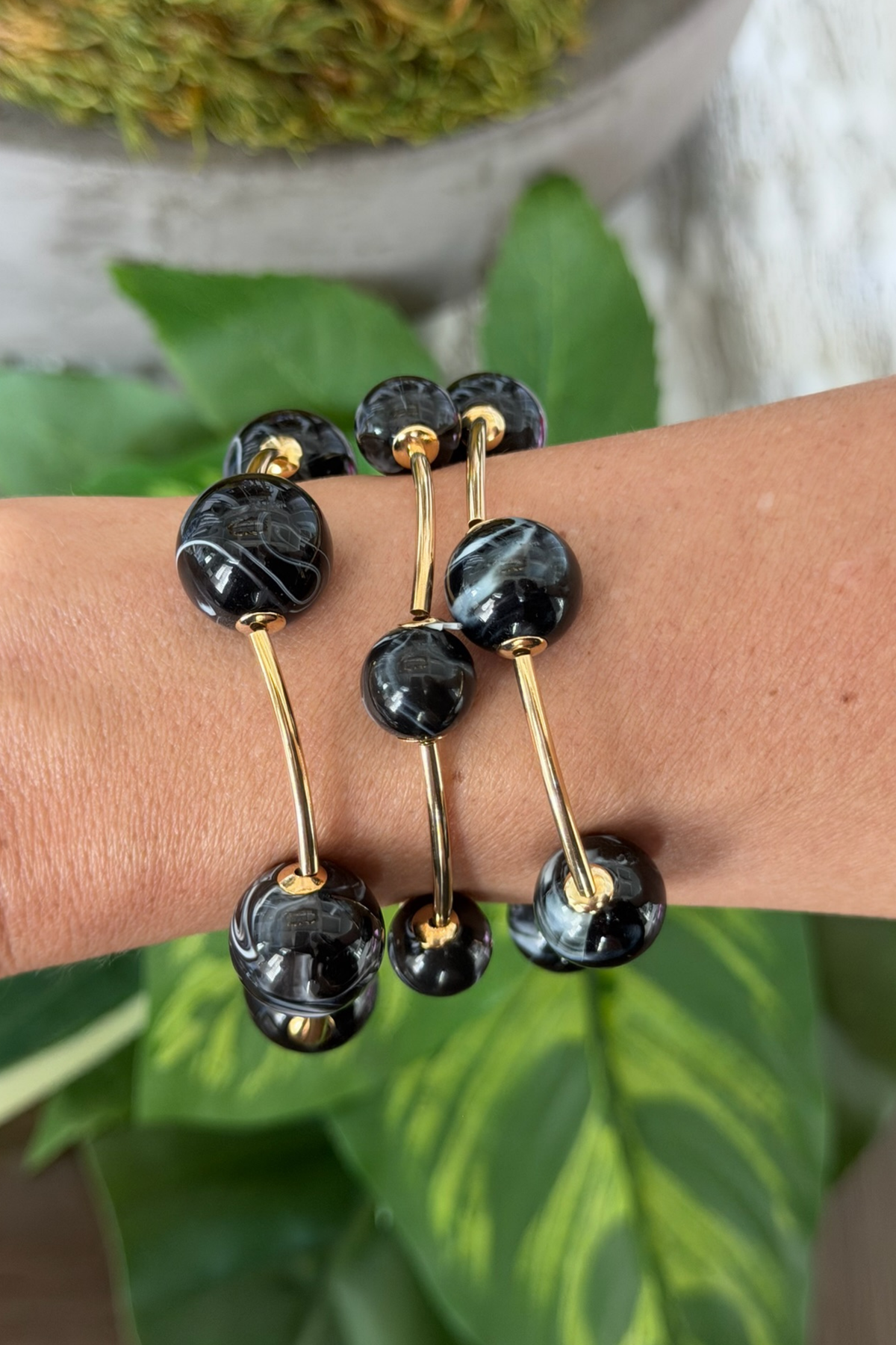 Black and gold bracelet on a wrist with green leaves in the background
