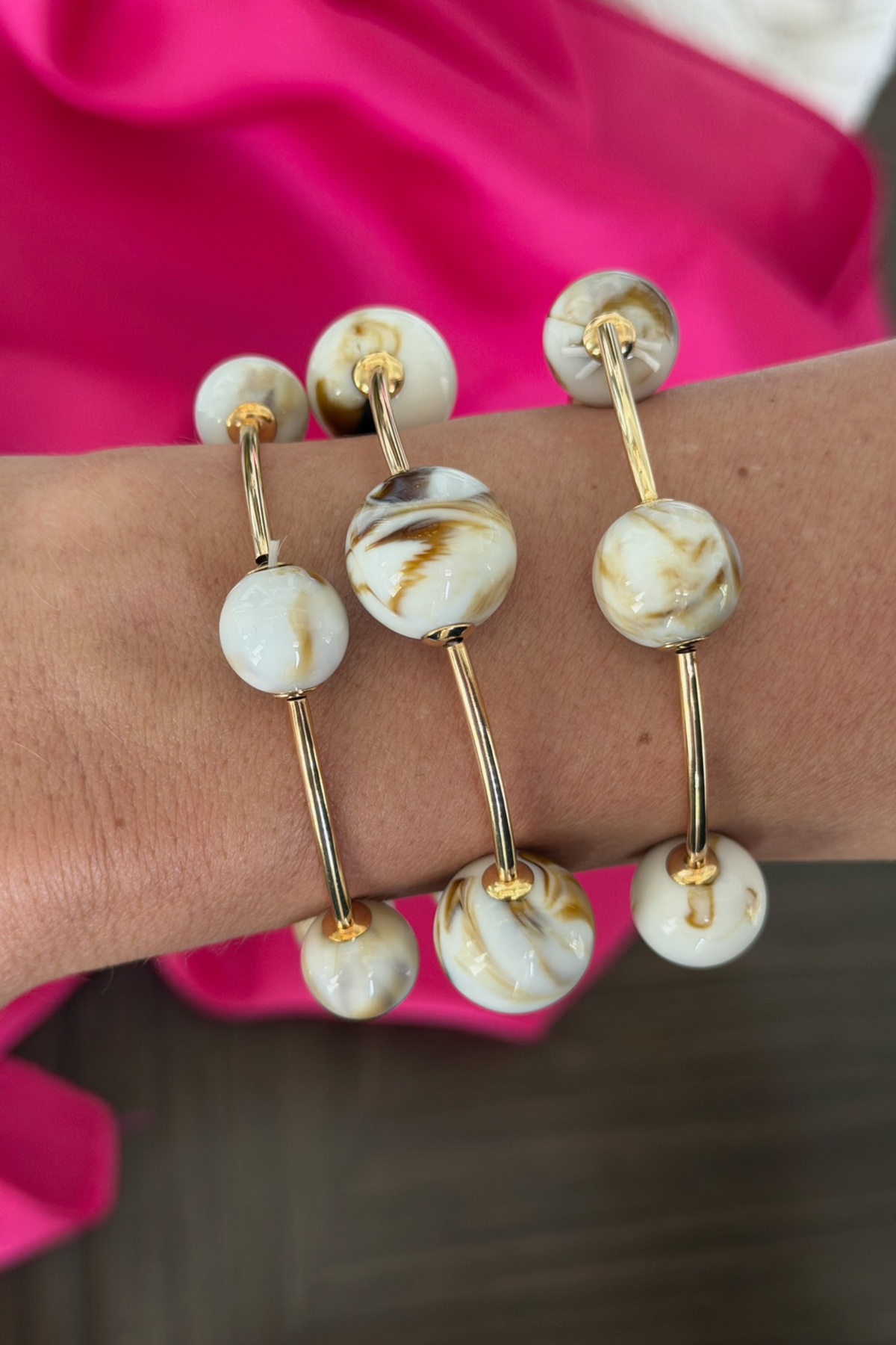 Bracelet with gold and white beads on a wrist against a pink fabric background