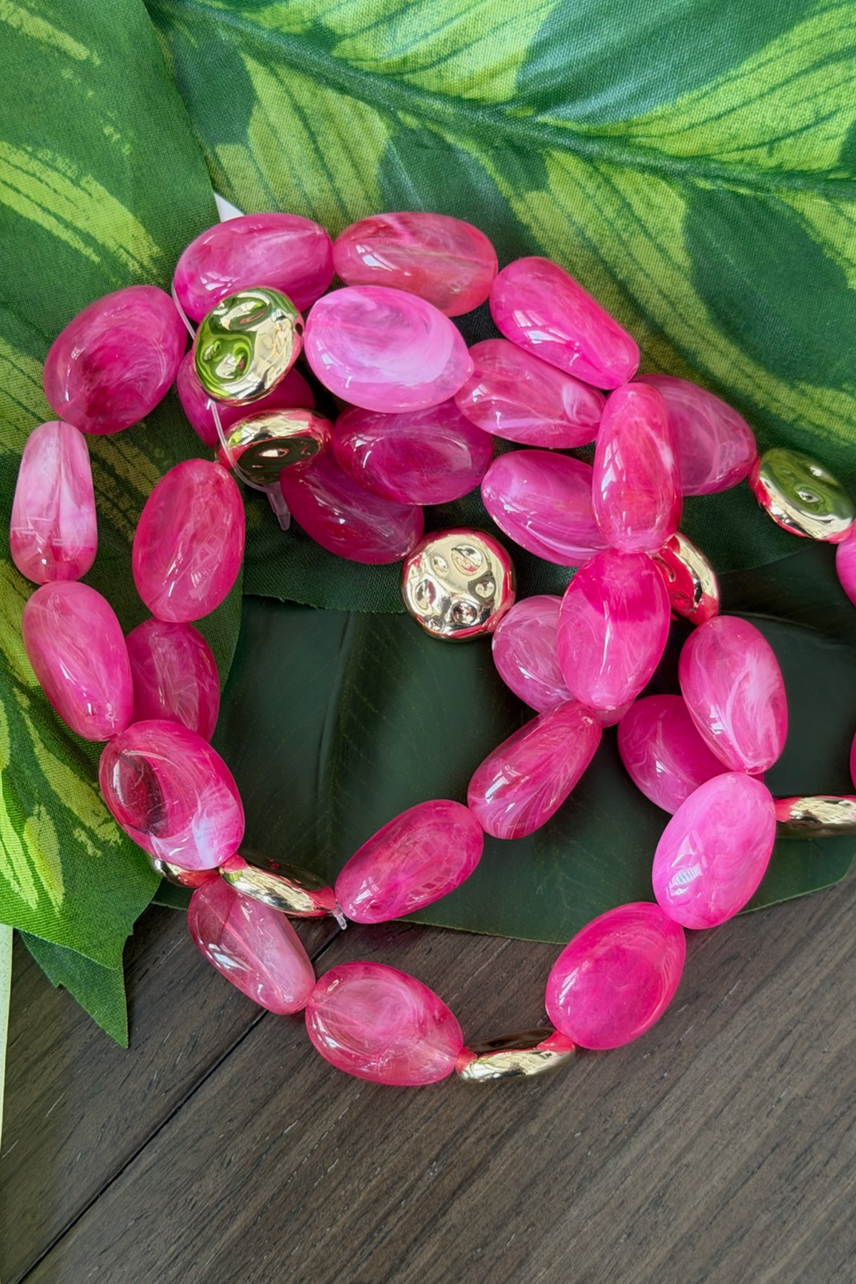 Pink beaded bracelet with gold accents on a green leaf background