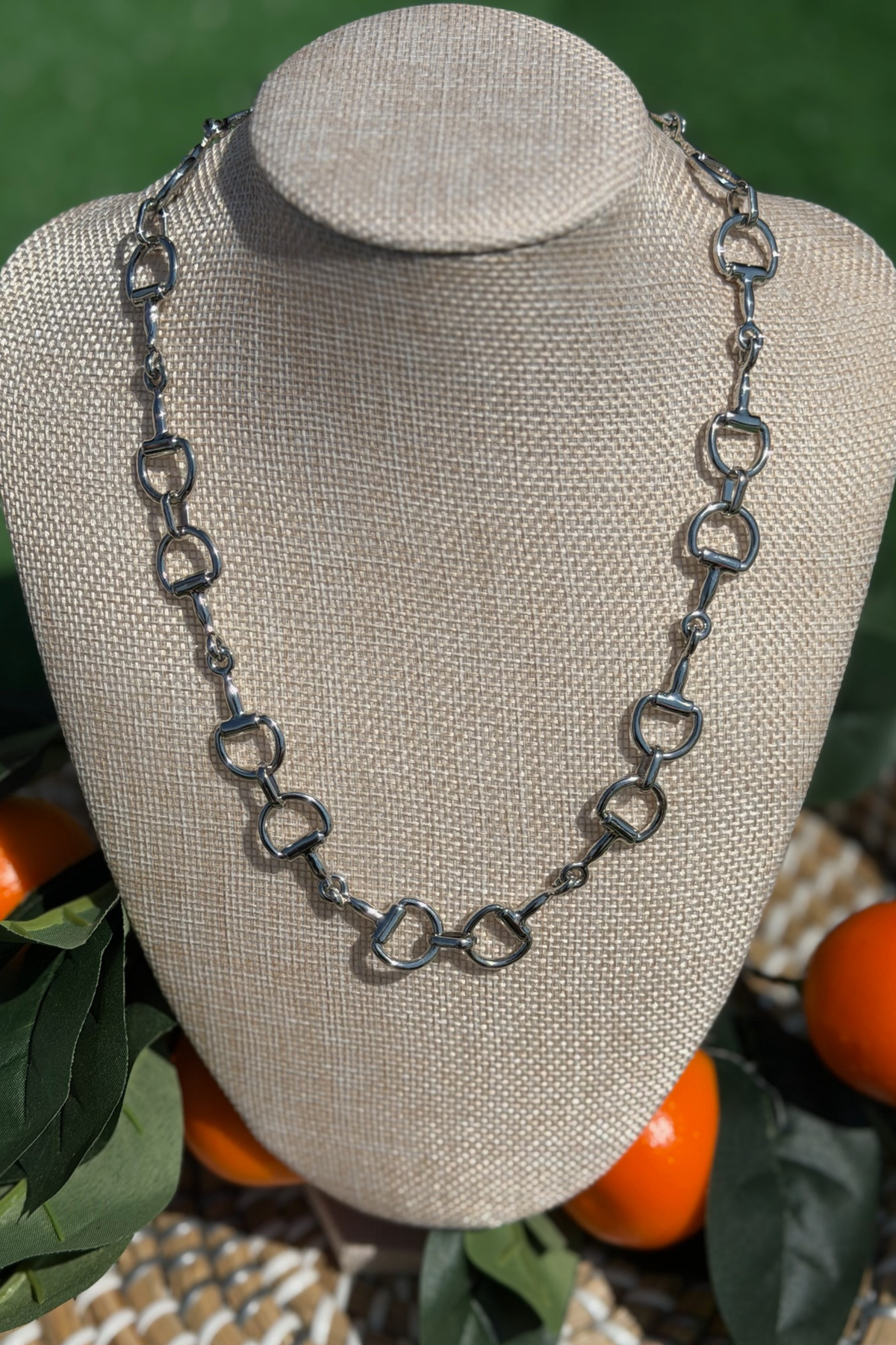 Silver chain necklace on a mannequin bust with orange fruits and green leaves in the background