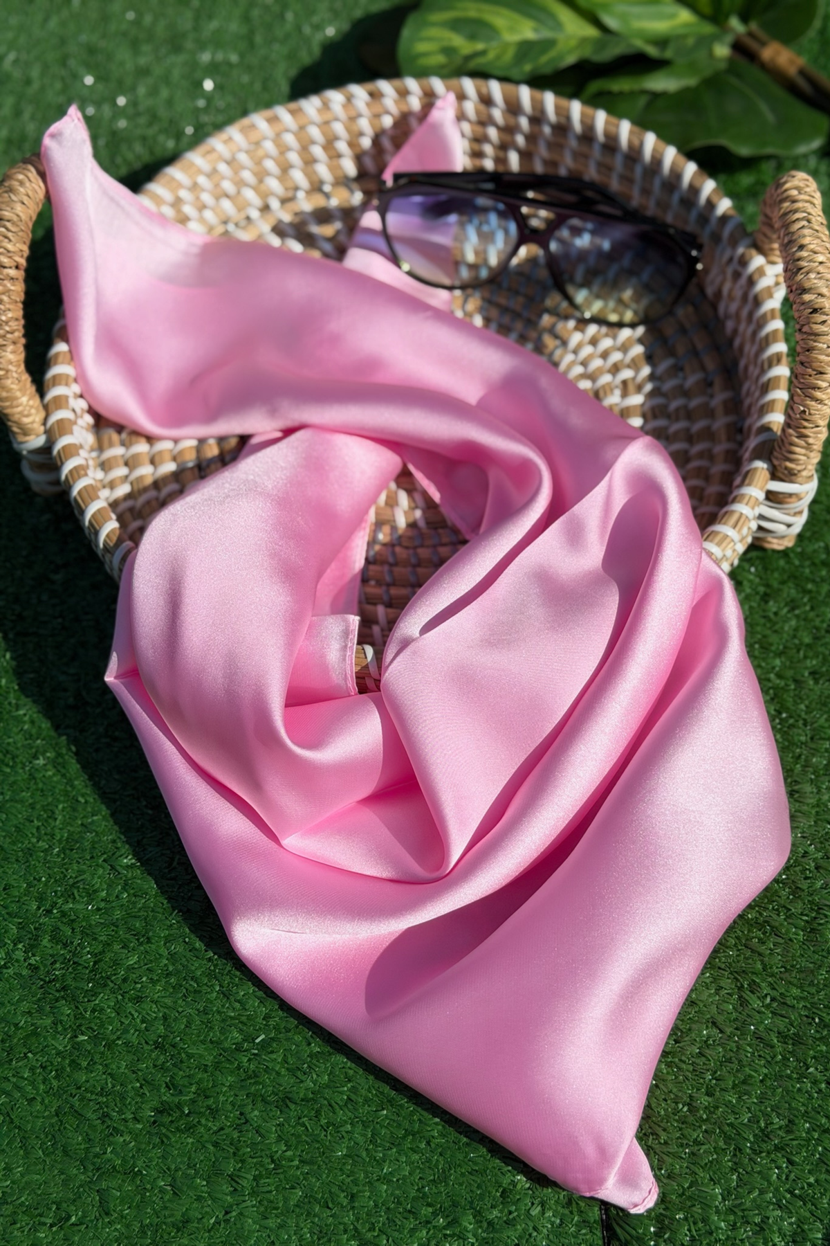Pink scarf draped over a woven basket with glasses on a green surface