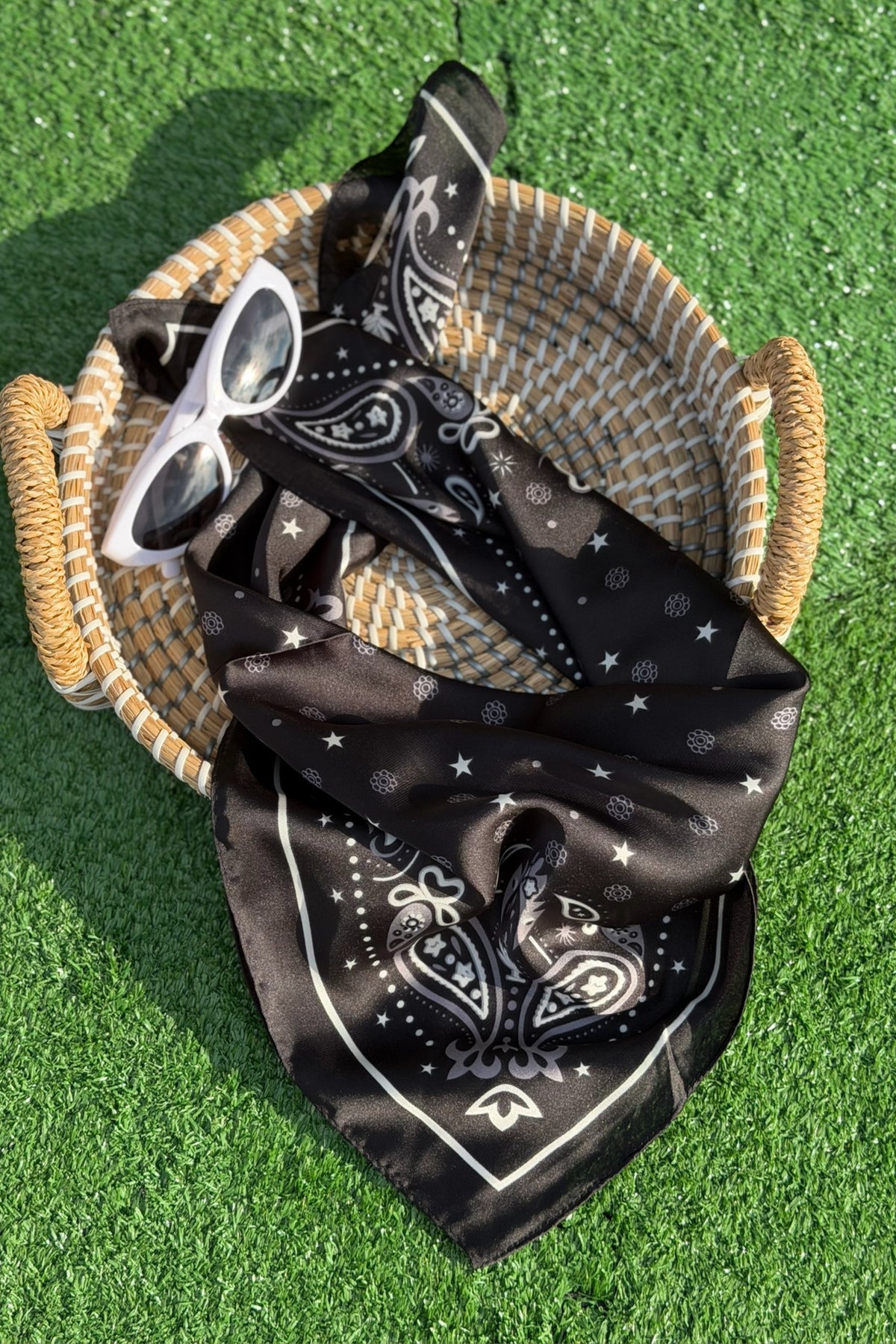 Black bandana with white patterns draped over a woven basket on green grass